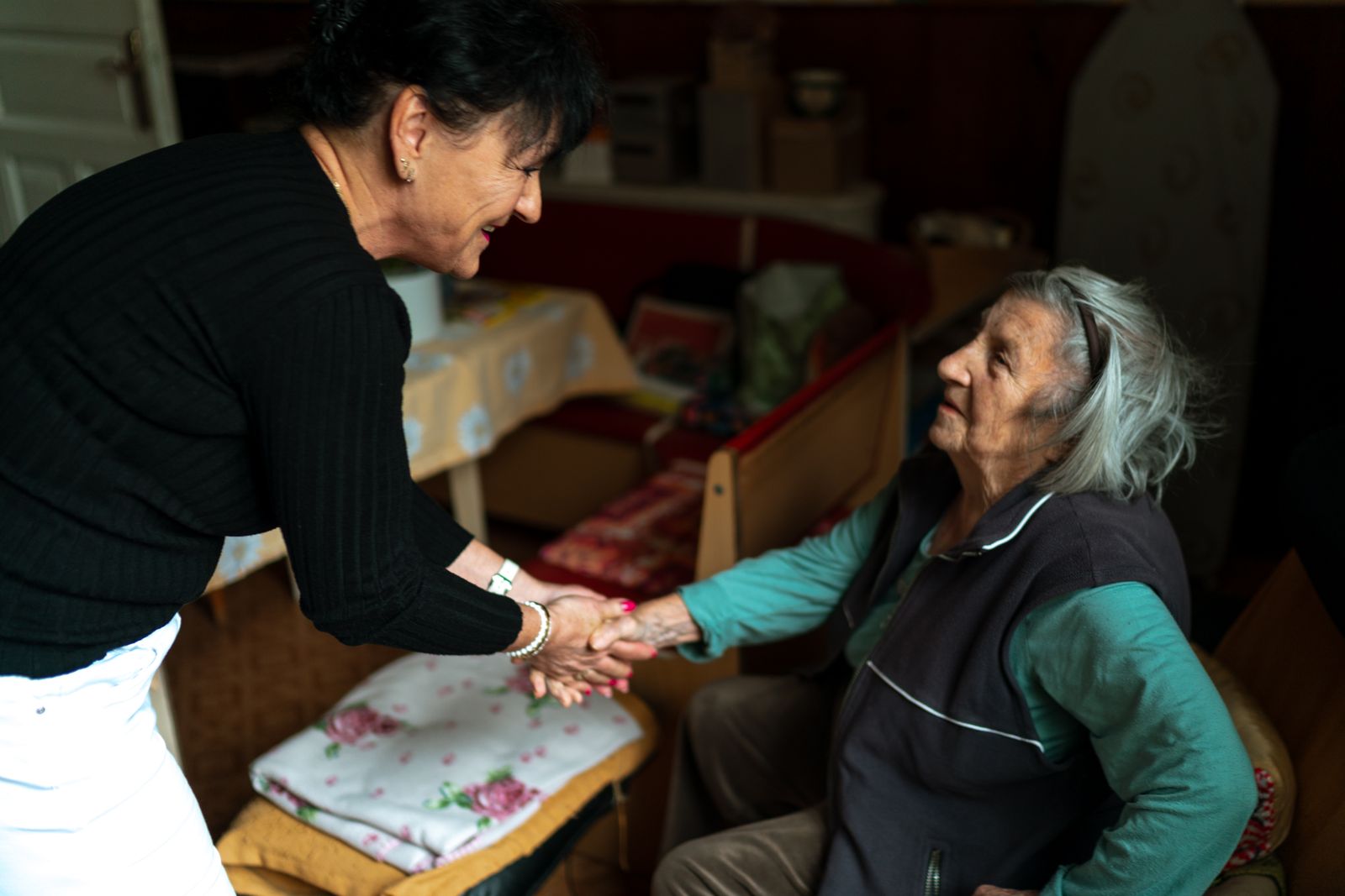 Two women greeting each other beside a chair at home
