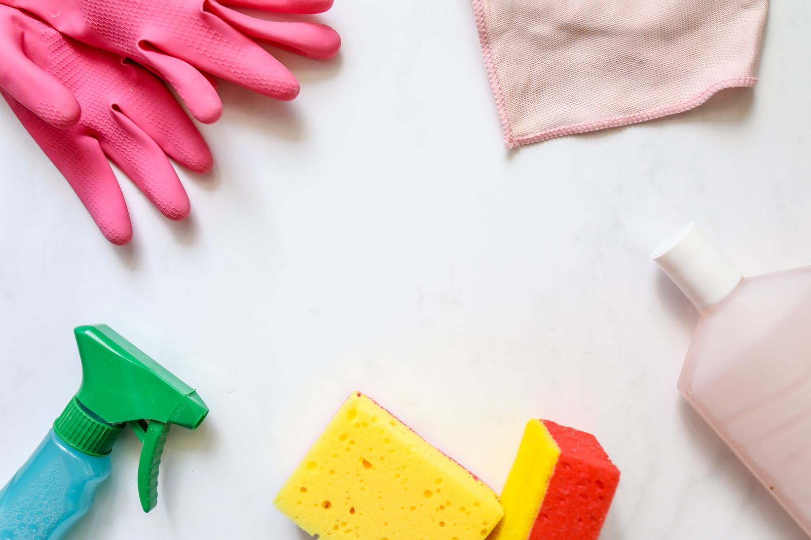 Gloves, sponges, a cloth and a spray bottle on a white surface