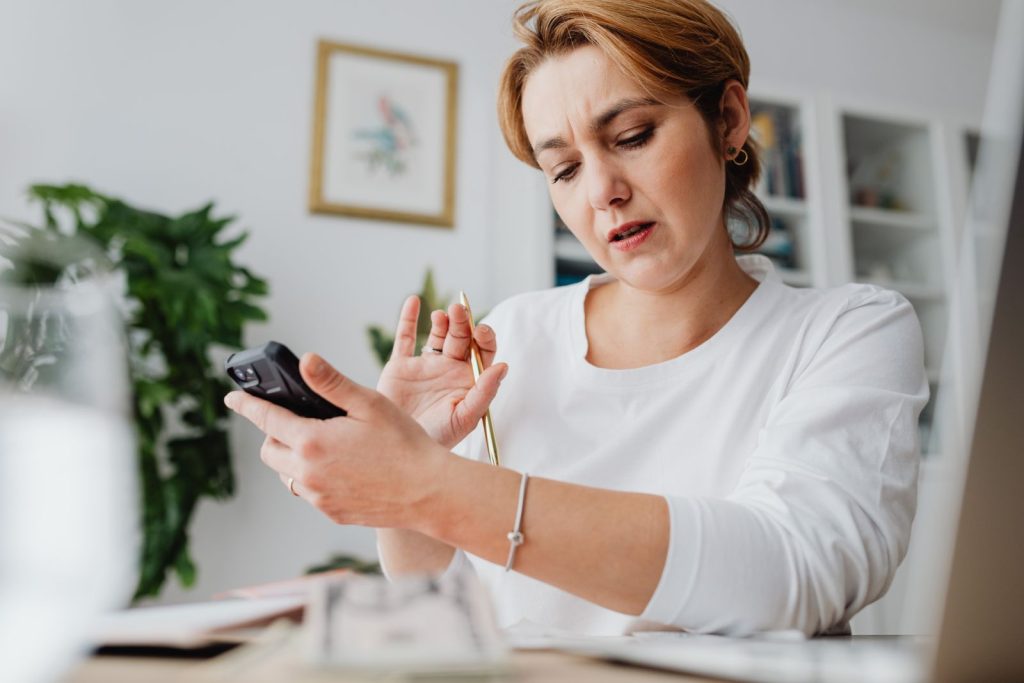A woman using a smartphone beside a laptop