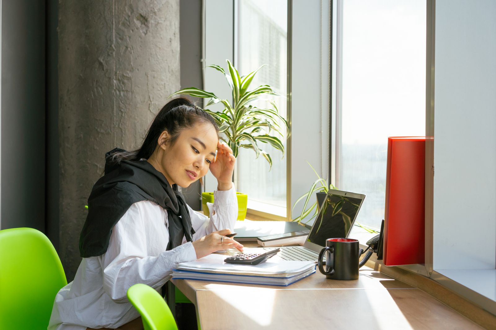 A woman writing at a desk beside an open laptop